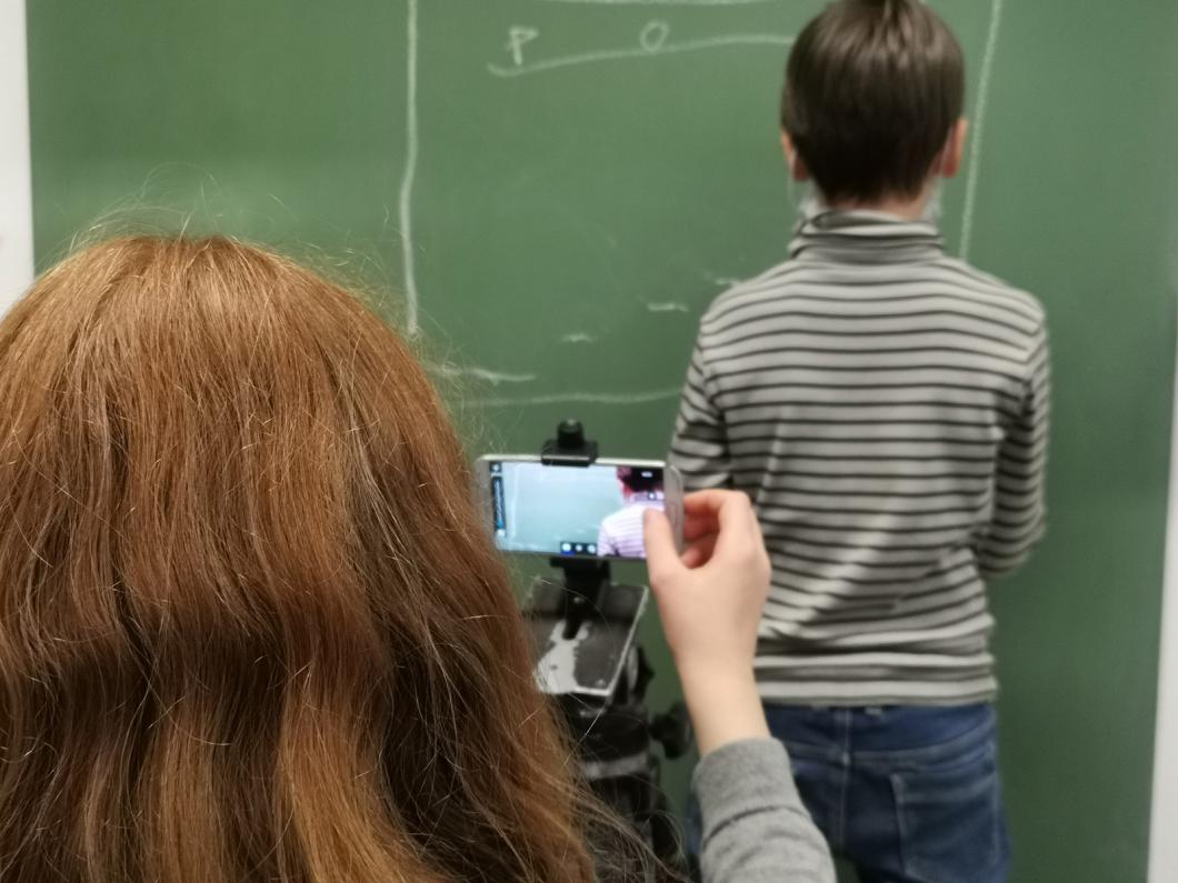 Ein Kind filmt ein anderes vor einer Tafel